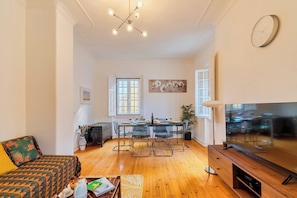 Una sala moderna con un sofá, una mesa de comedor con sillas, un televisor y una araña.