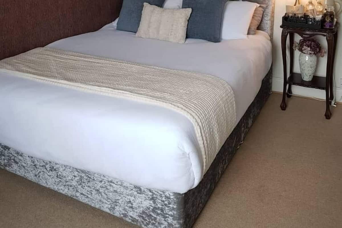 A neatly made bed with a headboard, a bedside table with a lamp, and a vase with flowers.
