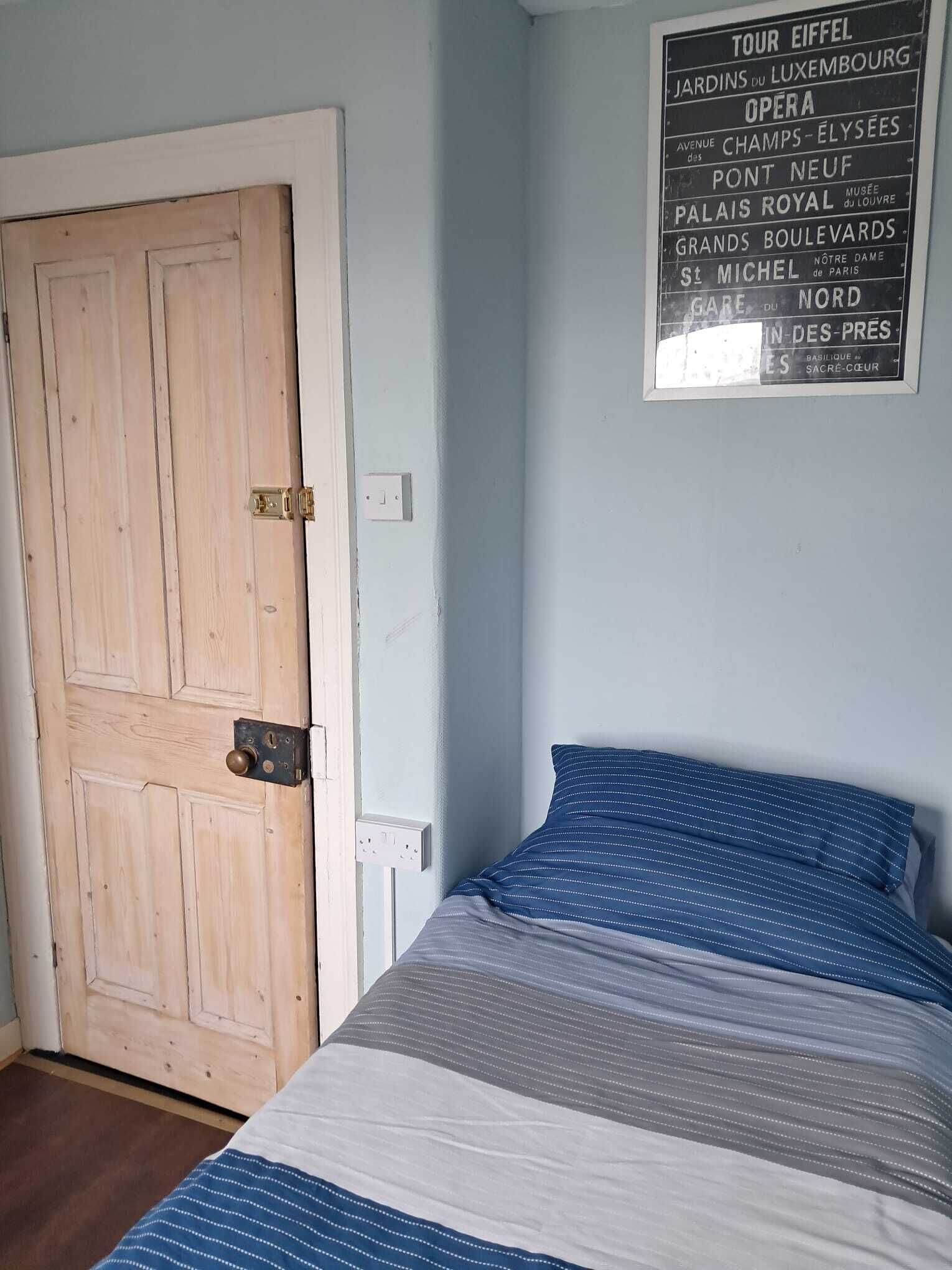 A bedroom with a bed, a wooden door, and a wall with a sign listing Paris landmarks.