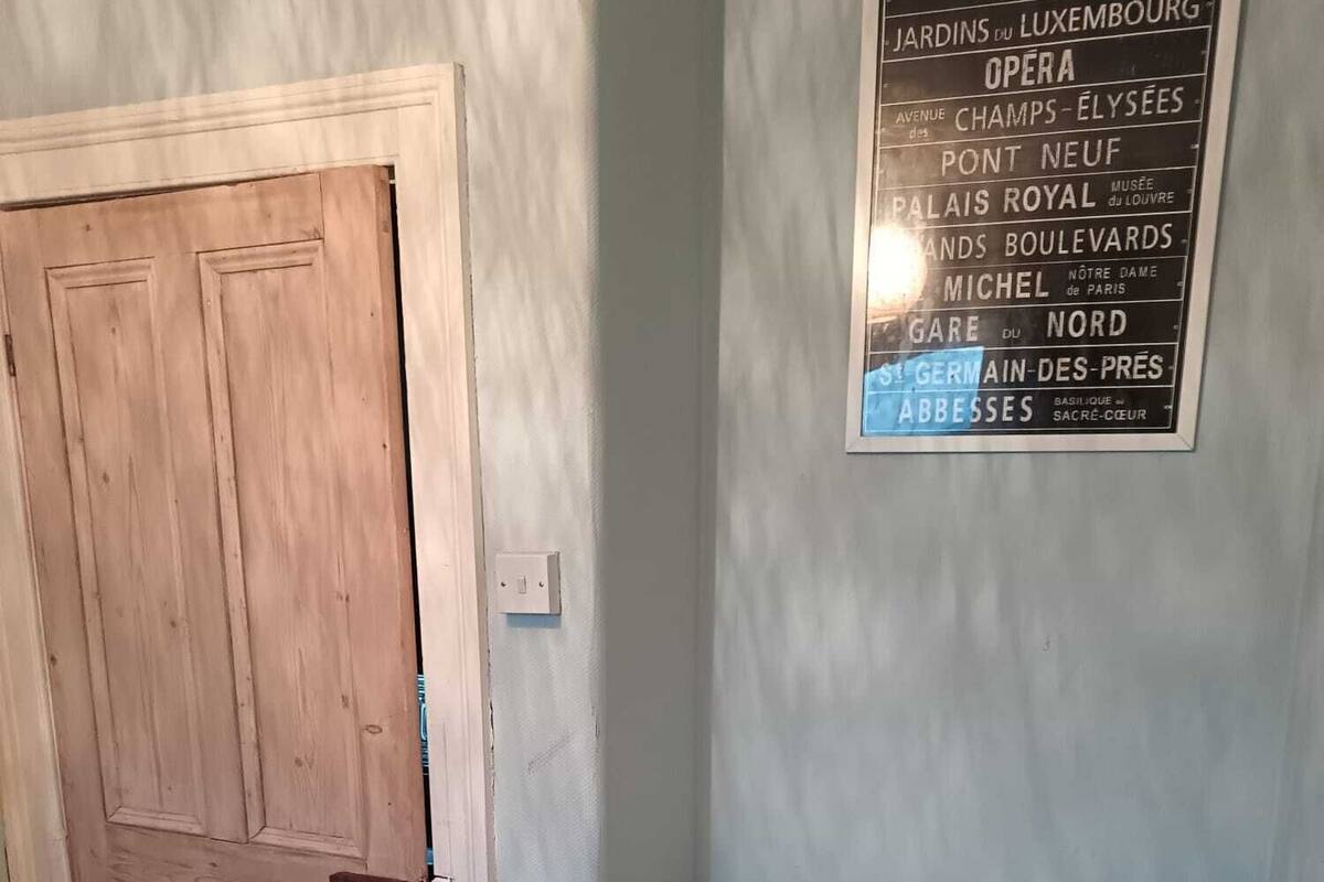 A bedroom with a bed, a wooden door, and a wall with a list of Parisian landmarks.