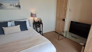 Un dormitorio con cama, mesita de noche con lámpara, televisor y puerta.