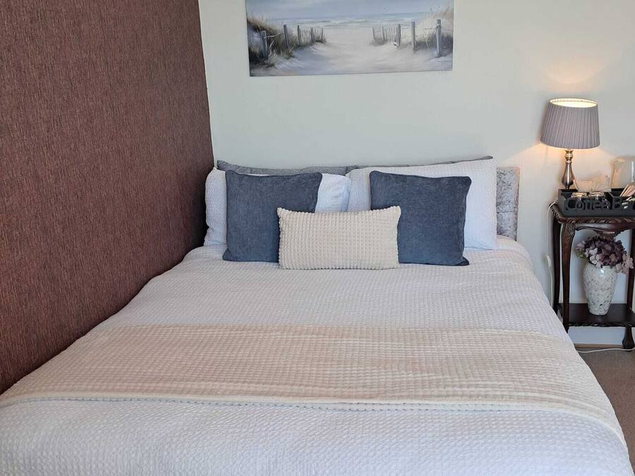 Une chambre à coucher avec un lit, une table de chevet avec une lampe, un tableau au mur et une vue sur l’extérieur.