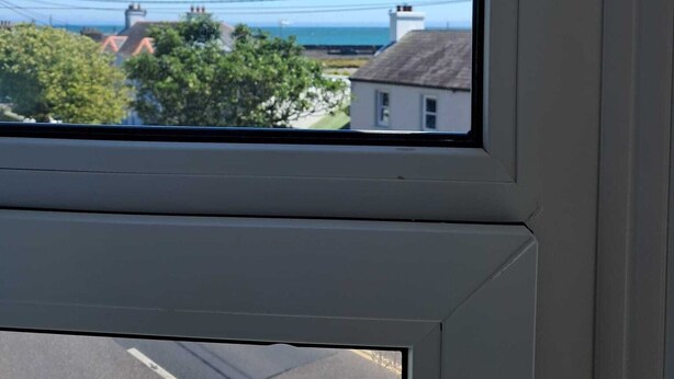 Una ventana con vistas despejadas a una carretera y edificios, incluyendo una casa de fachada blanca y una chimenea.