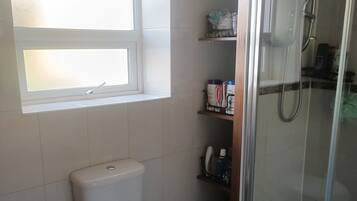 A bathroom with a toilet, a shower enclosure, a window, and shelves with toiletries.