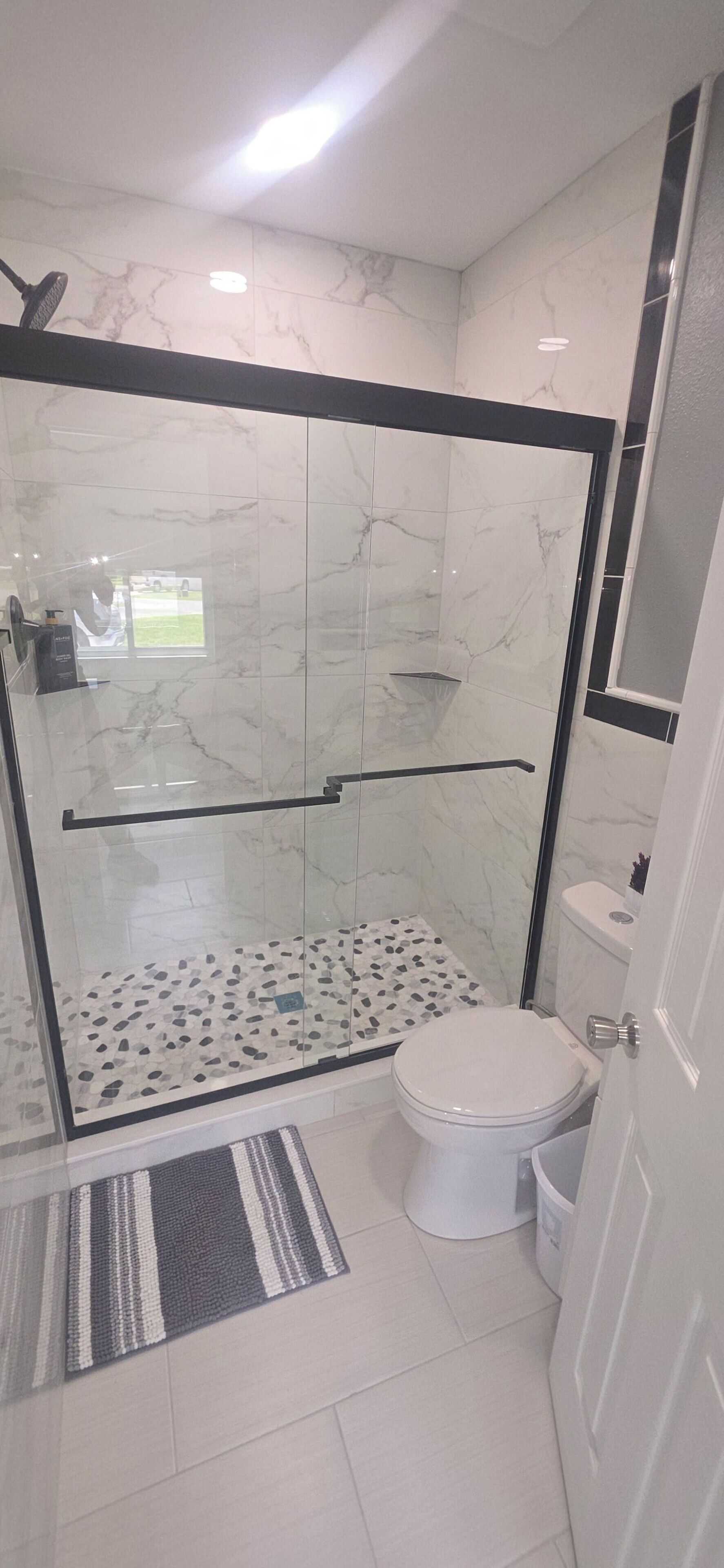 A bathroom with a glass-enclosed shower, a toilet, and a small rug.