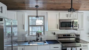 A modern kitchen with white cabinets, a stainless steel refrigerator, a double sink, a microwave, and a large oven. - Horse-Friendly Retreat:Trail Access, Woodland Views & Peaceful Deck (Allardt)