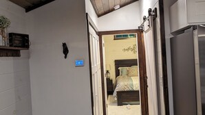 A narrow hallway with a wooden ceiling, a yellow rug, a bed with a patterned bedspread, and a refrigerator. - Horse-Friendly Retreat:Trail Access, Woodland Views & Peaceful Deck (Allardt)