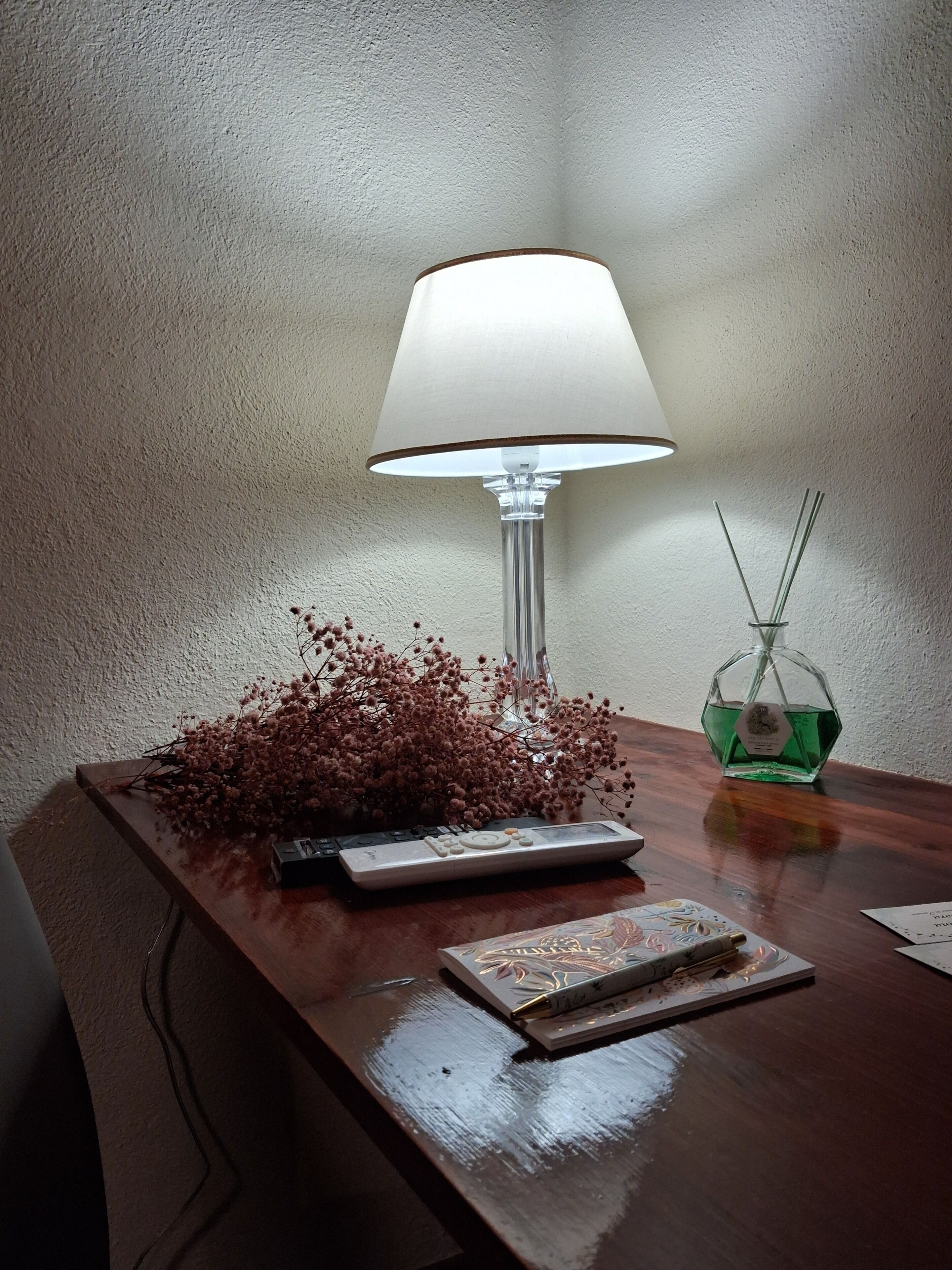 A desk with a lamp, a remote control, a decorative vase, and a small bottle.
