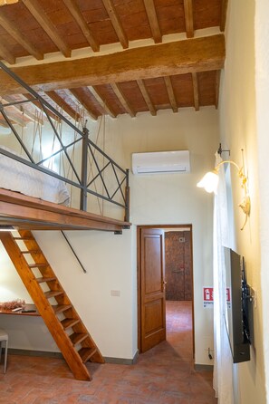 Ein Schlafzimmer im Loft-Stil mit einer Holztreppe, einer Klimaanlage und einer Tür zu einem weiteren Raum.