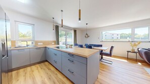 Una cocina moderna con una isla central, armarios grises y una zona de comedor con sillas azules.