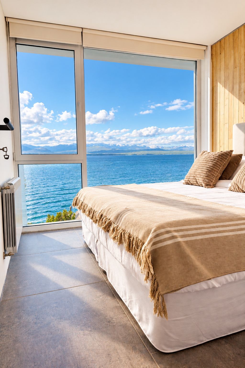 Ein Schlafzimmer mit großem Fenster mit Blick auf ein Gewässer und Berge.