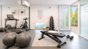 Un gimnasio moderno con equipo de ejercicio, una cinta de correr, bicicleta estática y un soporte de mancuernas en la pared.