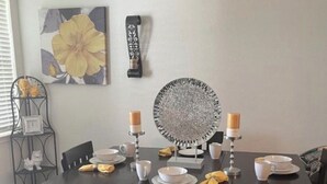 Ein Essbereich mit einem schwarzen Tisch, gedeckt für sechs Personen, umgeben von schwarzen Stühlen. In der Mitte liegt ein dekorativer Teller, auf jeder Seite zwei Kerzen und eine Wanduhr.
