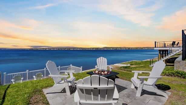 A lakeside patio with Adirondack chairs, a fire pit, and a deck overlooking the water. - Waterfront Cottage (Swansea)