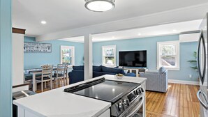 A modern kitchen with a gas stove, dining area with chairs and a table, a living room with a sofa and TV, and a large window. - Waterfront Cottage (Swansea)