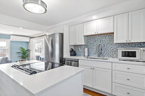 A modern kitchen with white cabinets, stainless steel appliances, and a patterned backsplash. - Waterfront Cottage (Swansea)