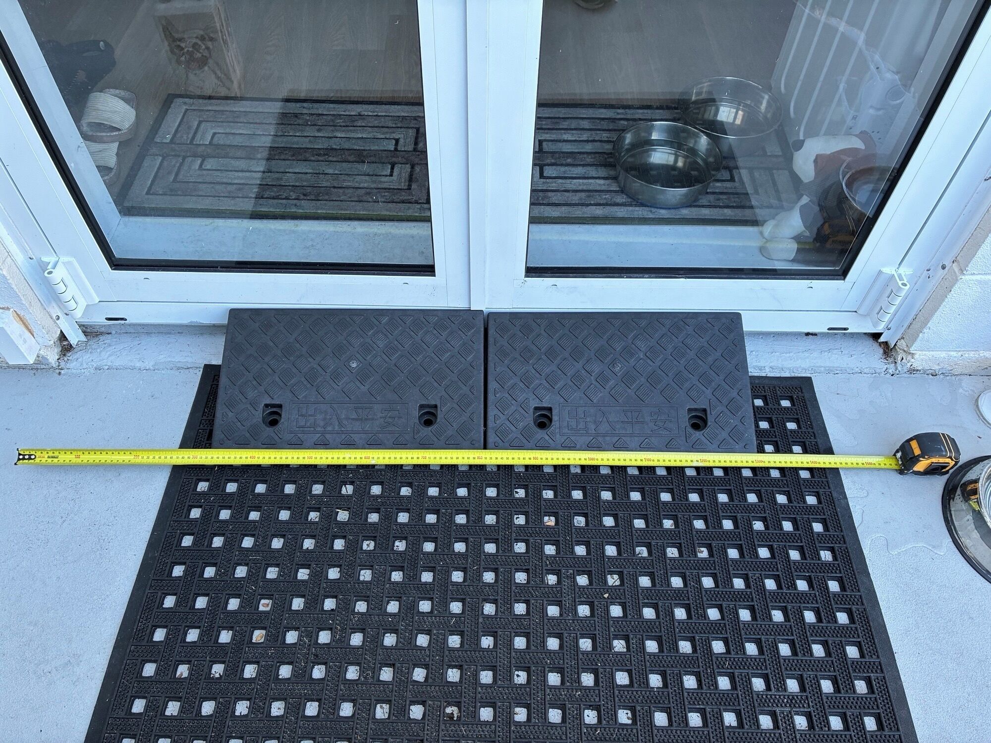 Une porte avec un paillasson noir et un mètre ruban jaune posé dessus.
