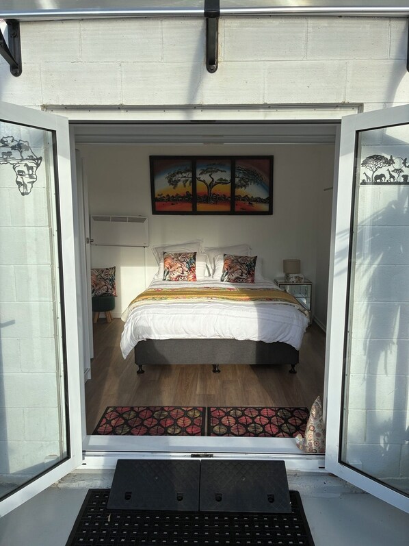 Un dormitorio con una cama, almohadas, una mesita de noche, una lámpara y un cuadro en la pared.