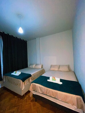 Ein Zimmer mit zwei Betten, einer Deckenleuchte und Holzboden.