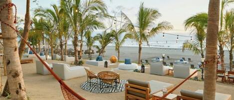 A beachside lounge area with seating, a hammock, and palm trees.