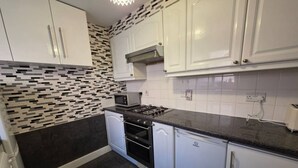 A compact kitchen with white cabinets, a gas stove, a microwave, and a tiled backsplash.