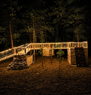 Eine Holzkonstruktion mit Hängebrücke und Kletterwand, umgeben von Bäumen.