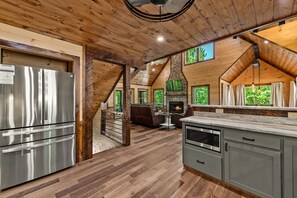 Eine moderne Küche mit Kamin aus Stein, Holzboden und großen Fenstern.
