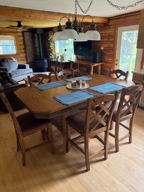 A wooden dining table with chairs, a television, and a fireplace in a cabin-style room.