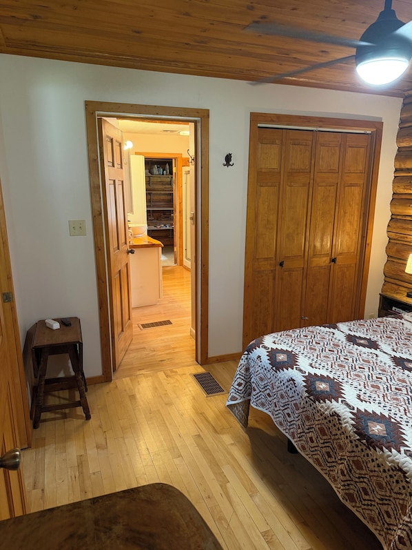 Une pièce au plancher de bois, avec un lit, une armoire et une petite table.