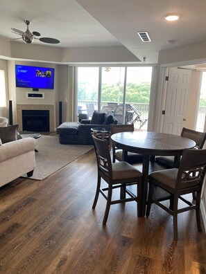 Un salon avec une cheminée, un téléviseur fixé au mur, une table à manger avec des chaises et un balcon aménagé avec du mobilier d’extérieur.