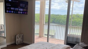 A bedroom with a large bed, a TV mounted on the wall, and a balcony with a view of greenery. - 5100 Towers Beautiful Condo! Quiet! Elevators, indoor/outdoor pools. Free Wifi (Osage Beach)