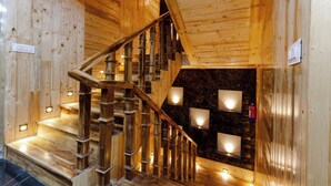 Una escalera de madera con barandilla que conduce a una habitación con pared de piedra oscura e iluminación empotrada.