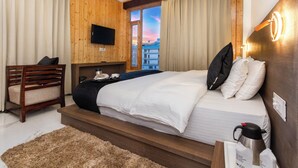 Habitación de hotel con cama, televisión, cabecero de madera, una silla y vistas a la ciudad.