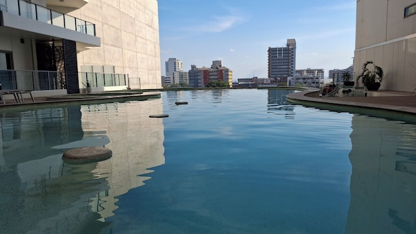 A swimming pool with clear water, surrounded by modern buildings, some with balconies. - 1-bedroom apartment, Darwin city with sunset and harbour views for family of 4 (Darwin City)