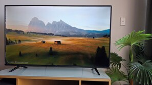 A flat-screen TV on a wooden stand with a scenic landscape image. - 1-bedroom apartment, Darwin city with sunset and harbour views for family of 4 (Darwin City)