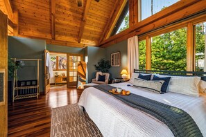 A wooden ceiling, a bed with pillows, a nightstand, a window with a view of trees, and a door leading to another room. - Private Wellness Retreat | Epic Mtn Views + Sauna (Sevierville)