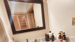 Une salle de bain avec un lavabo en marbre, des meubles en bois, un grand miroir et des articles de toilette posés sur le comptoir.