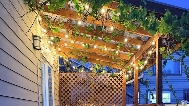 A wooden deck with a table and chairs, a wooden railing, and a lattice wall. - Lynnwood Retreat: Office, Theater & Grapevine Deck (Lynnwood)
