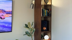 A corner room with a wooden bookshelf, a mounted TV, a potted plant, and a speaker. - Lynnwood Retreat: Office, Theater & Grapevine Deck (Lynnwood)