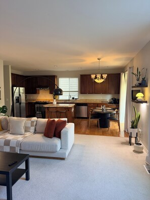 A modern living room with a sofa, a dining table, and a kitchen in the background. - Lynnwood Retreat: Office, Theater & Grapevine Deck (Lynnwood)