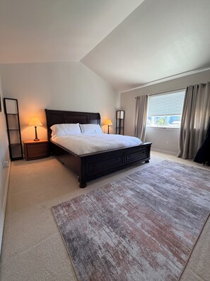 A bedroom with a large bed, two bedside tables with lamps, a window with curtains, and a view of the outside.