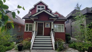 Uma casa de dois andares com fachada vermelha, varanda frontal e escada que leva à entrada.