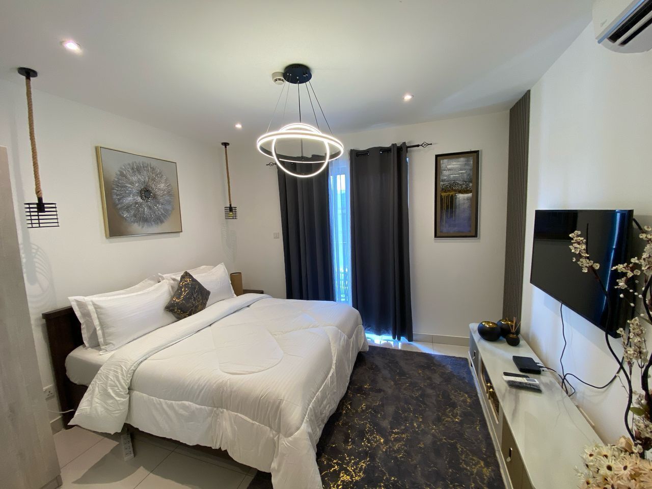A hotel room with a bed, a TV, a desk, and a window with curtains.