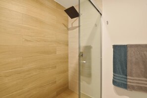 Een douche met glazen deur, houten vloer en een handdoekrek met twee handdoeken.