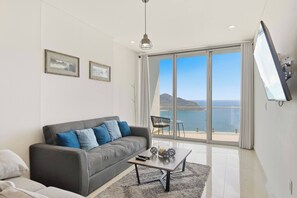Ein modernes Wohnzimmer mit einem grauen Sofa, einem Couchtisch und einem großen Fenster mit Meerblick.
