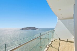 Ein Balkon mit Glasgeländer, der auf das Meer und eine kleine Insel Blick bietet.