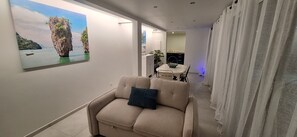 A modern interior with a beige sofa, a dining table, and a painting of a natural landscape on the wall. - Domaine du Paradis - Carambole Apartment (Le Robert)