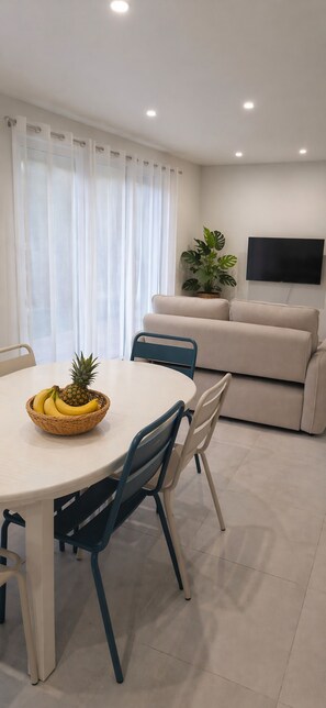 Ein modernes Wohnzimmer mit einem runden Esstisch, Stühlen, einer Couch, einem Fernseher und einer Topfpflanze.