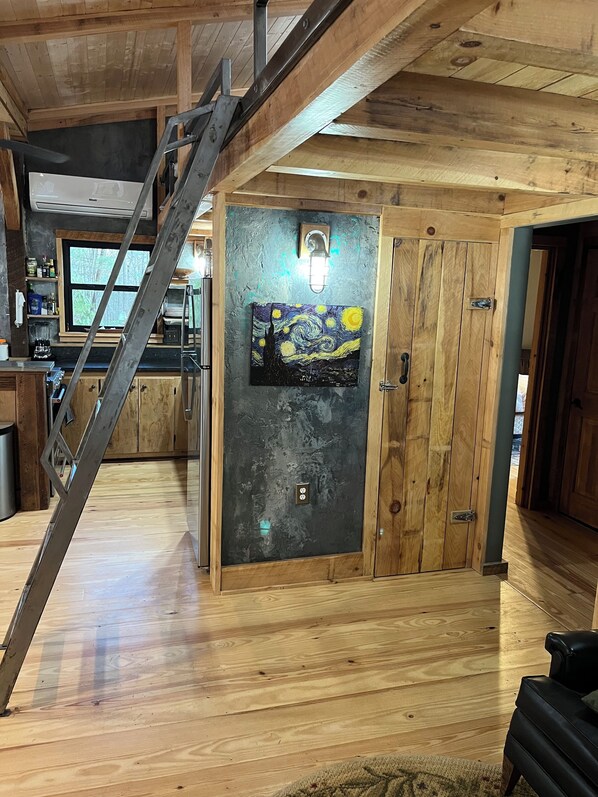 A rustic interior with wooden walls, a staircase, a kitchen area, and a painting on the wall.