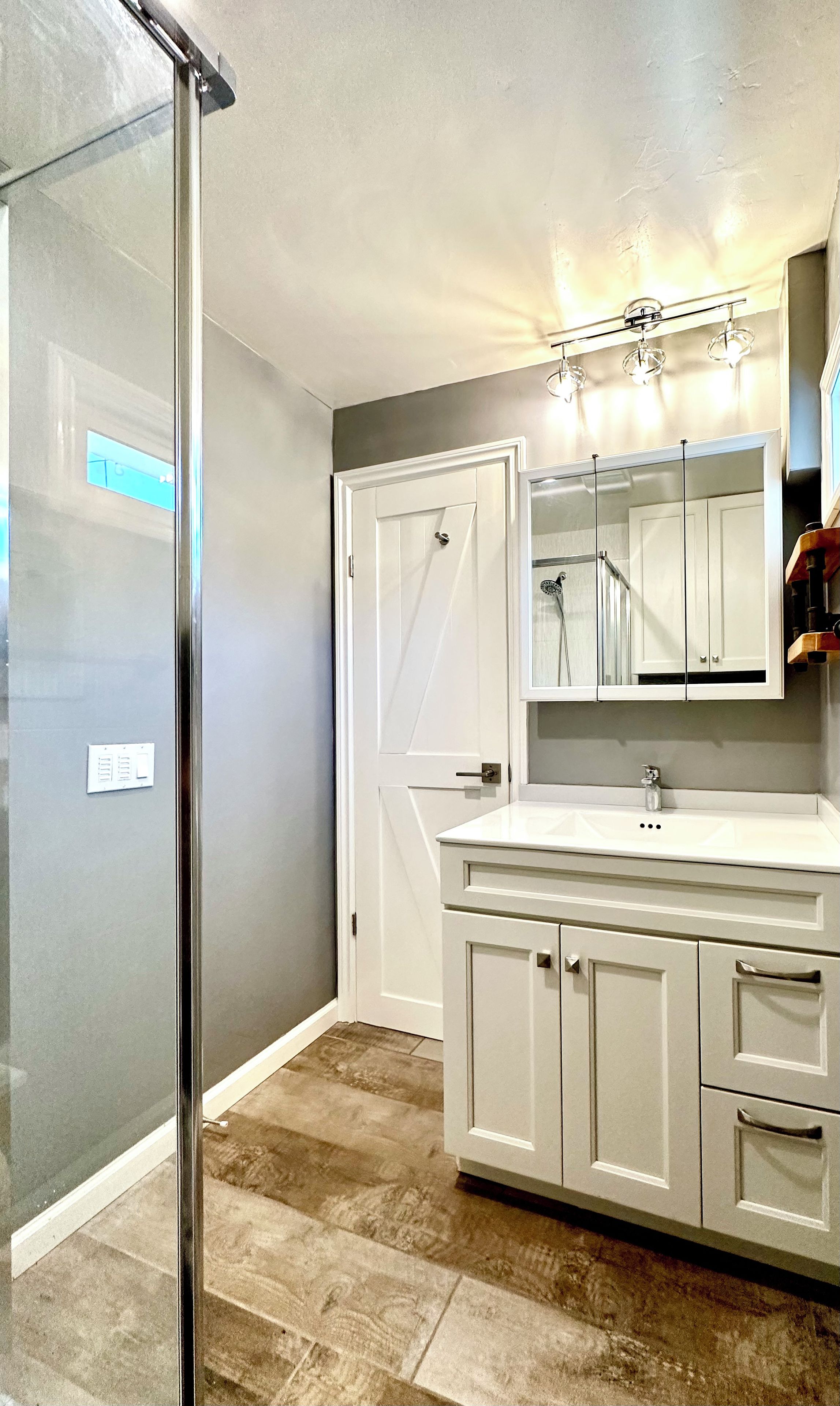 Une salle de bain avec une douche à parois de verre, un meuble-lavabo blanc avec un miroir et un luminaire placé au-dessus du miroir.